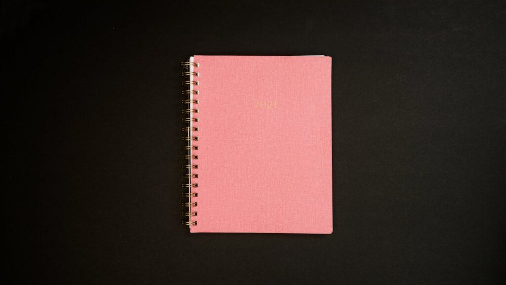 A stylish pink spiral notebook for 2021 on a black background, ideal for journaling or planning.